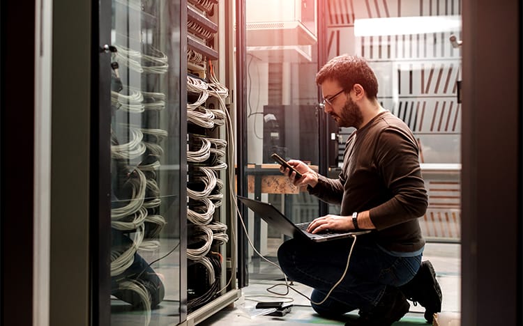 CAT’s Network Administration & Security Diploma program gets you ready for career success! Picture shows cyber security worker inspecting hardware in a server room. 