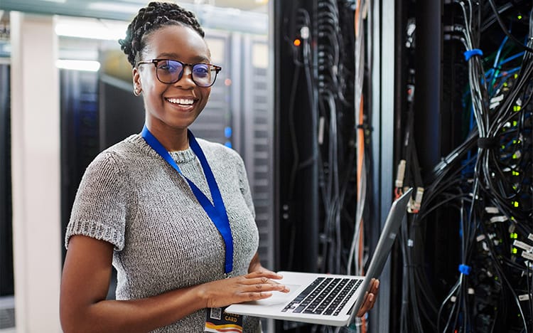CAT’s Network Administration & Security Diploma program gets you ready for career success! Picture shows cyber security worker smiling while working on a laptop in a server room.  