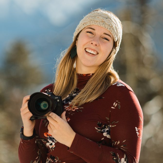 A woman holding a camera in front of mountains.