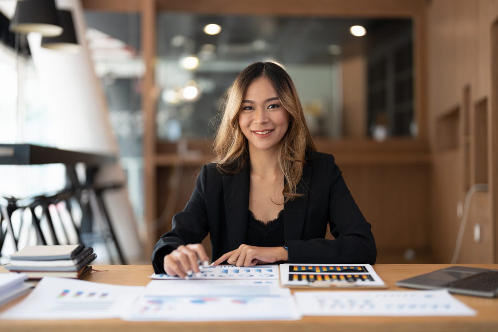 A young professional woman sits at a desk surrounded by spreadsheets and graphs.