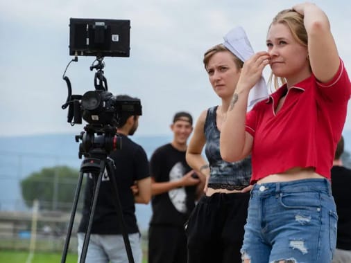 A group of College for Art and Design students are standing in front of a camera outdoors in summer.